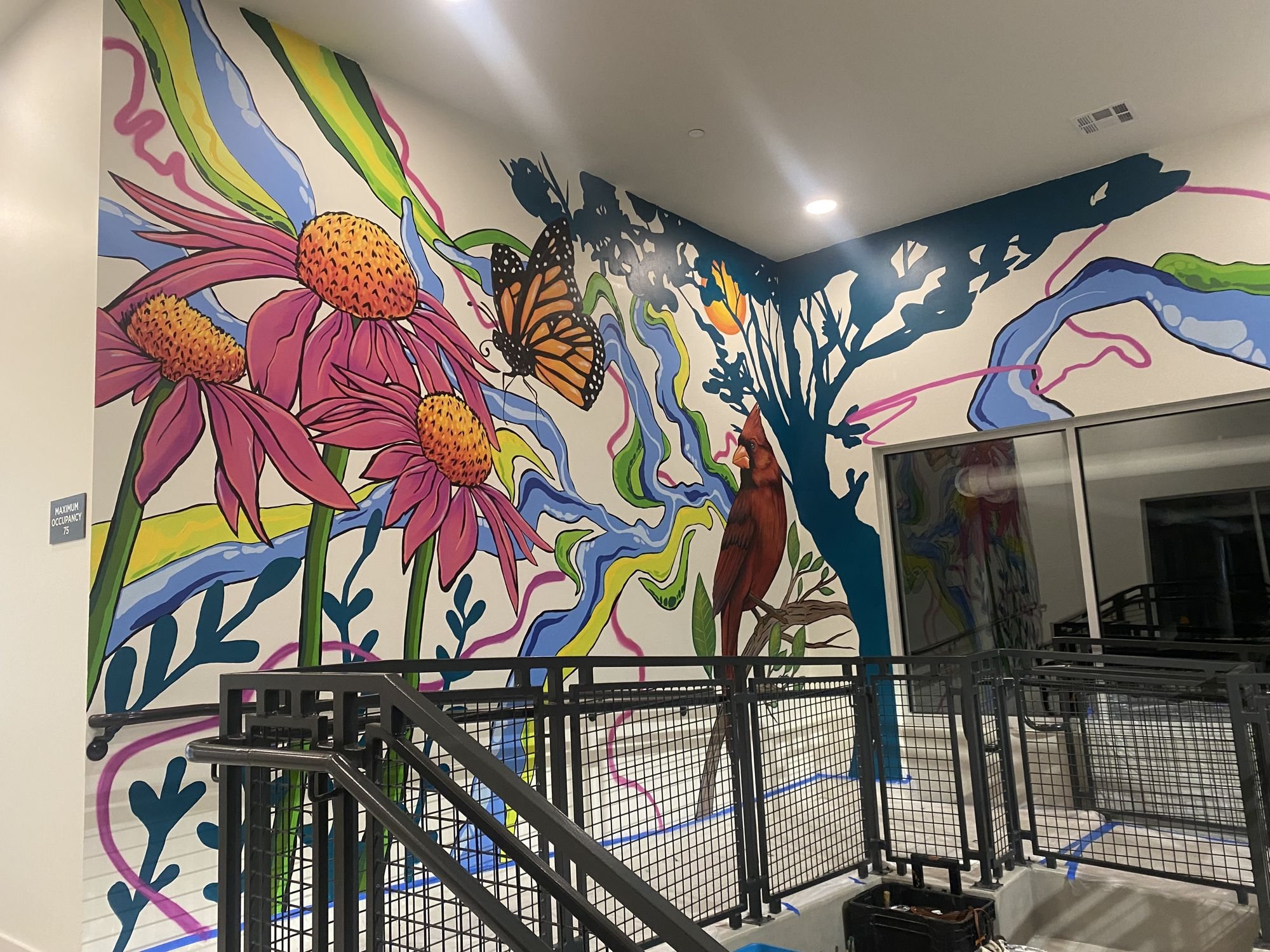 Large mural of coneflowers, a monarch butterfly, a cardinal and a blue tree wrapping an apartment stairwell
