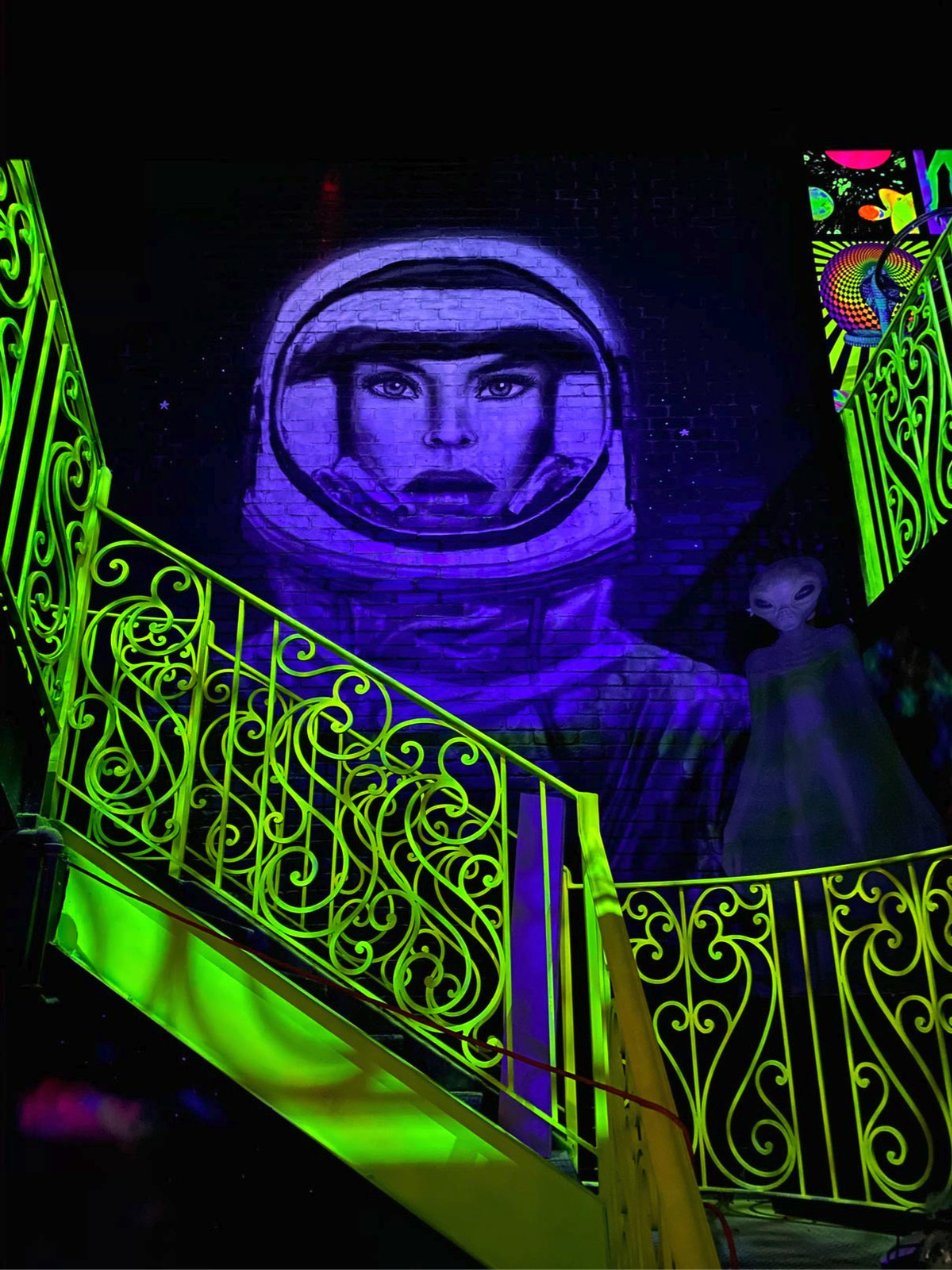 Glowing purple mural of an astronaut above neon green iron staircases in an event venue