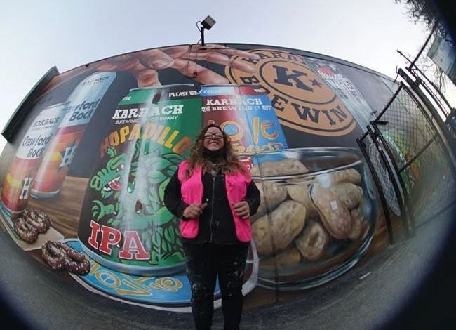 Sylvia Blanco standing in front of a large Karbach Brewing mural of beer cans and a jar of cookies