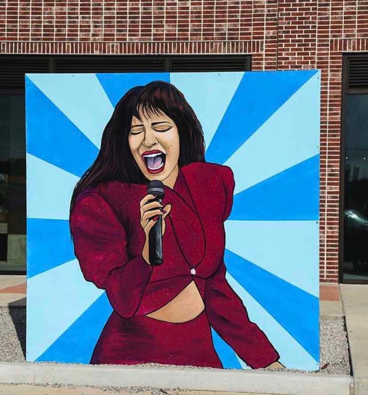 Portrait mural of Selena singing in a red outfit against a blue sunburst